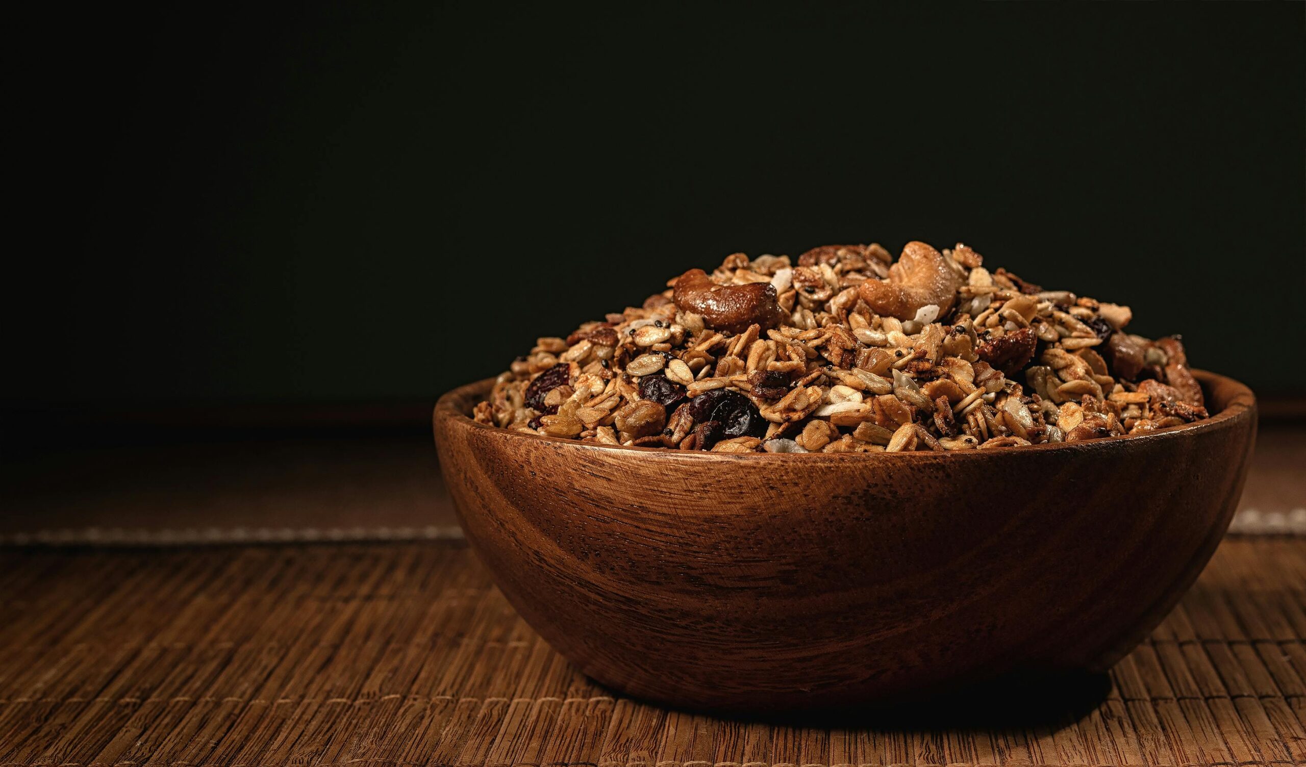 A rustic wooden bowl filled with nutritious granola, nuts, and seeds on a wooden surface.